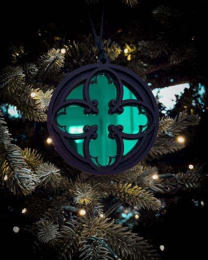 Green gothic cathedral quatrefoil ornament hanging on Christmas tree with warm lights
