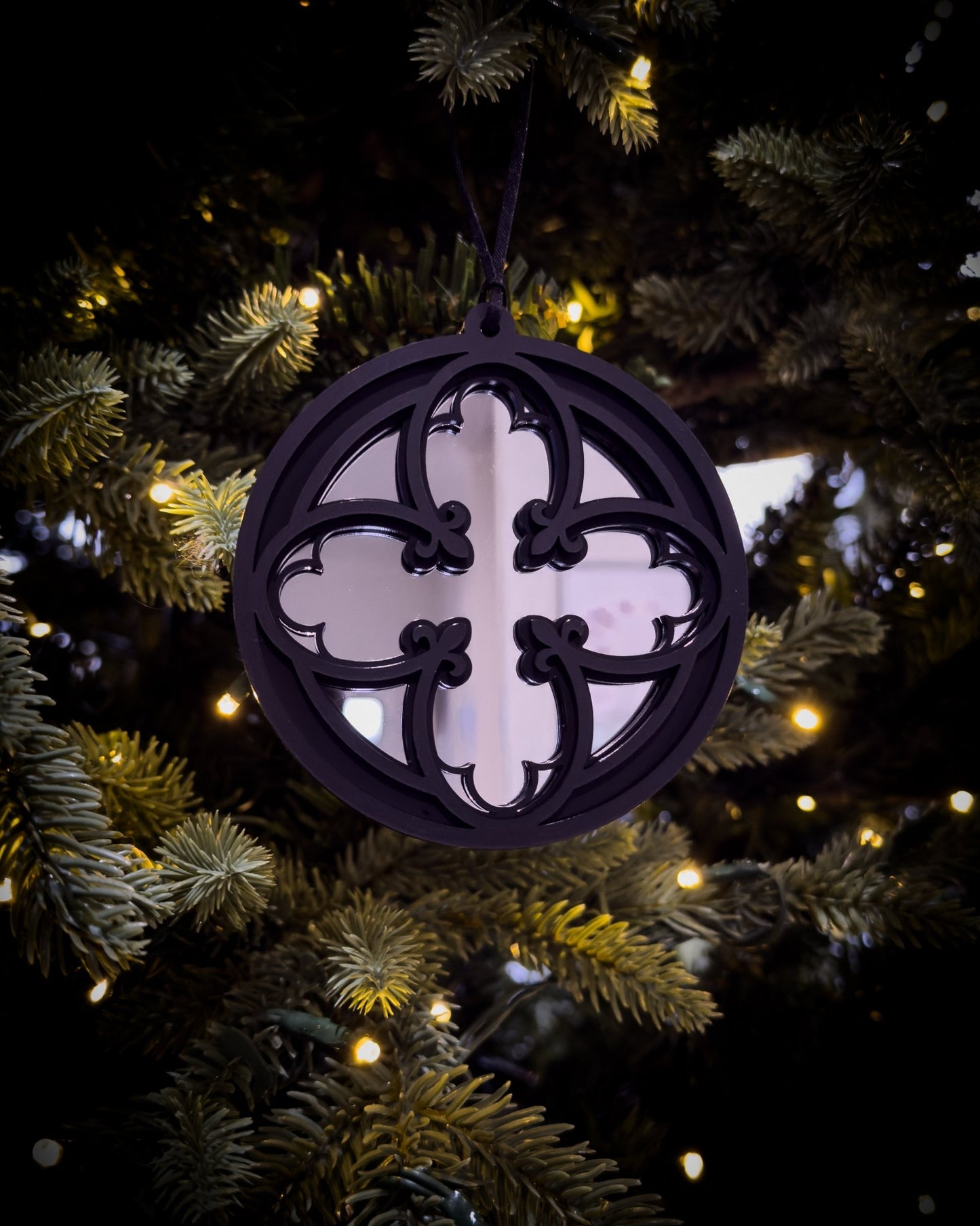 Silver gothic cathedral quatrefoil ornament hanging on Christmas tree with warm lights