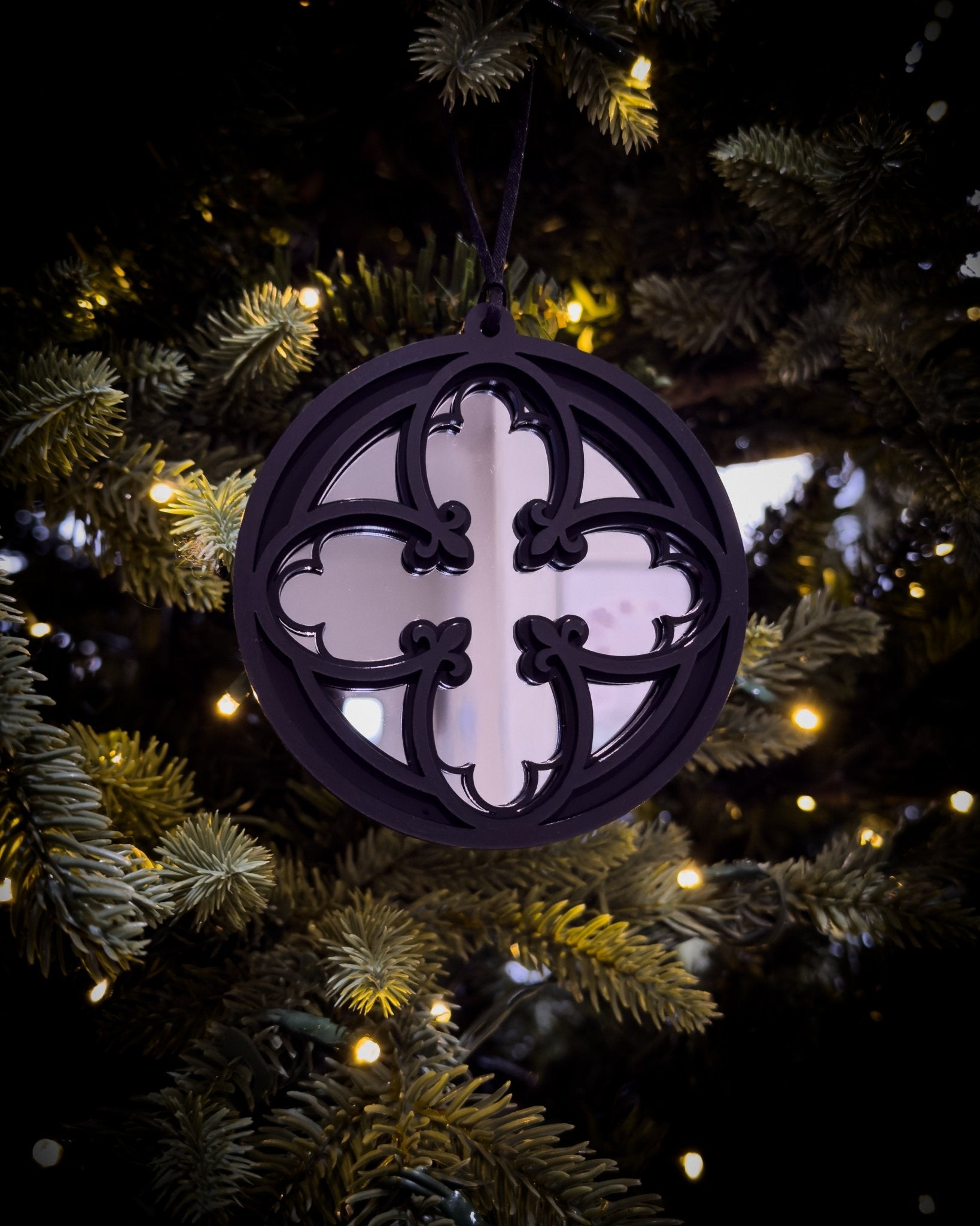 Silver gothic cathedral quatrefoil ornament hanging on Christmas tree with warm lights