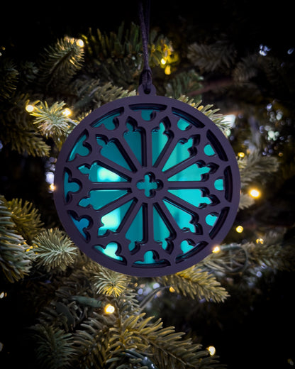 Green gothic cathedral rose window ornament hanging on Christmas tree with warm lights