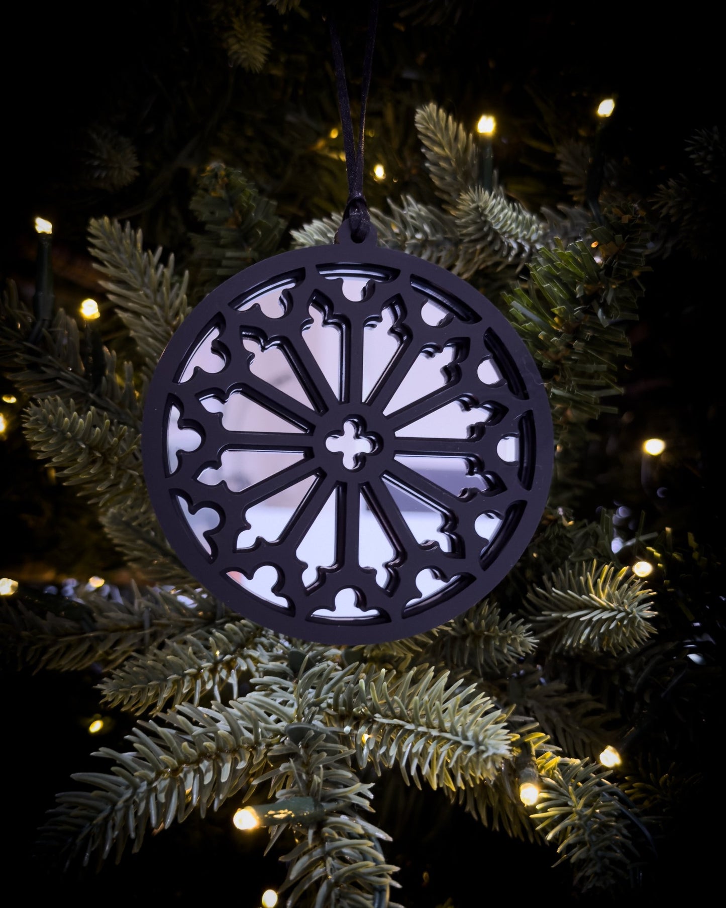 Silver gothic cathedral rose window ornament hanging on Christmas tree with warm lights