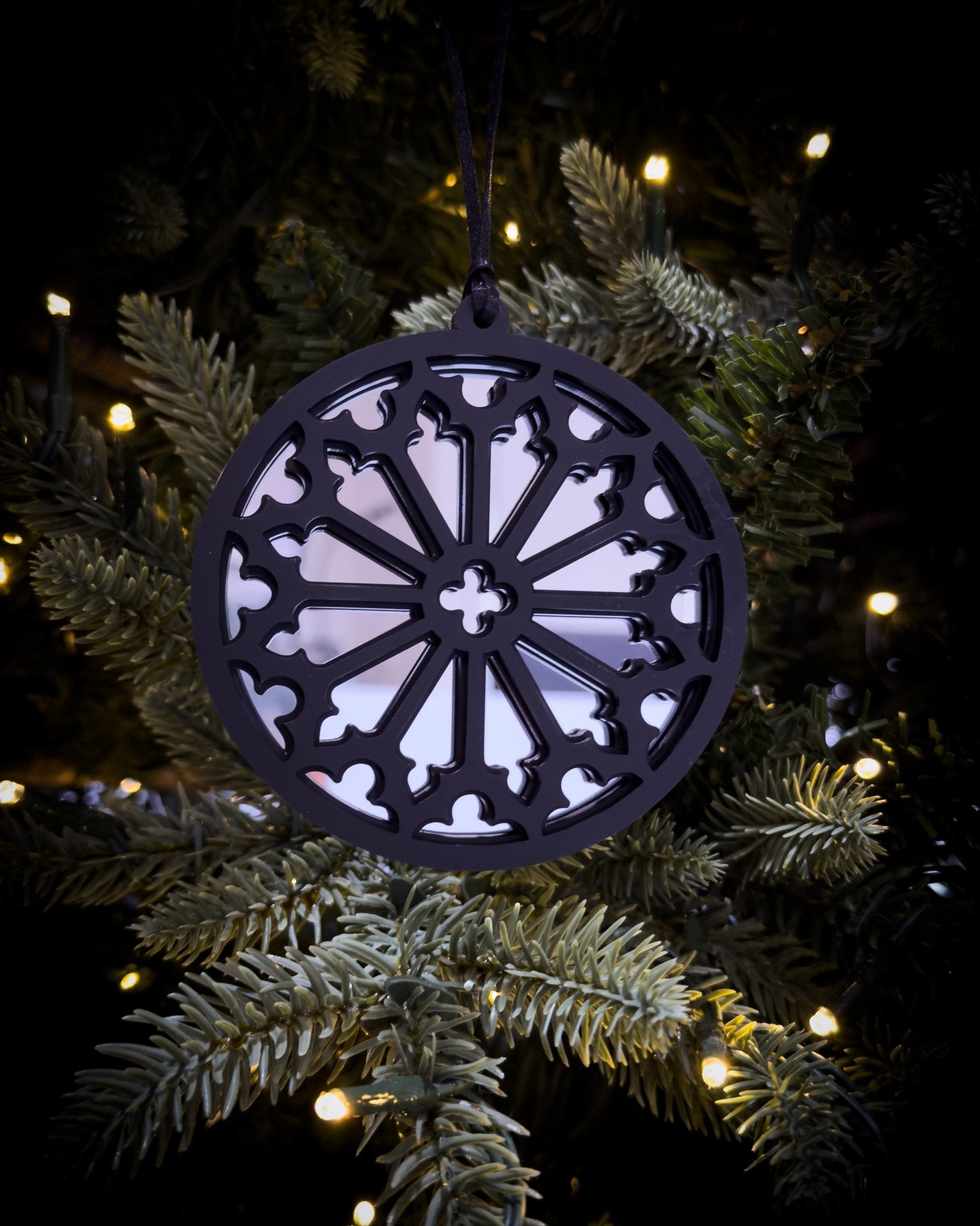 Silver gothic cathedral rose window ornament hanging on Christmas tree with warm lights