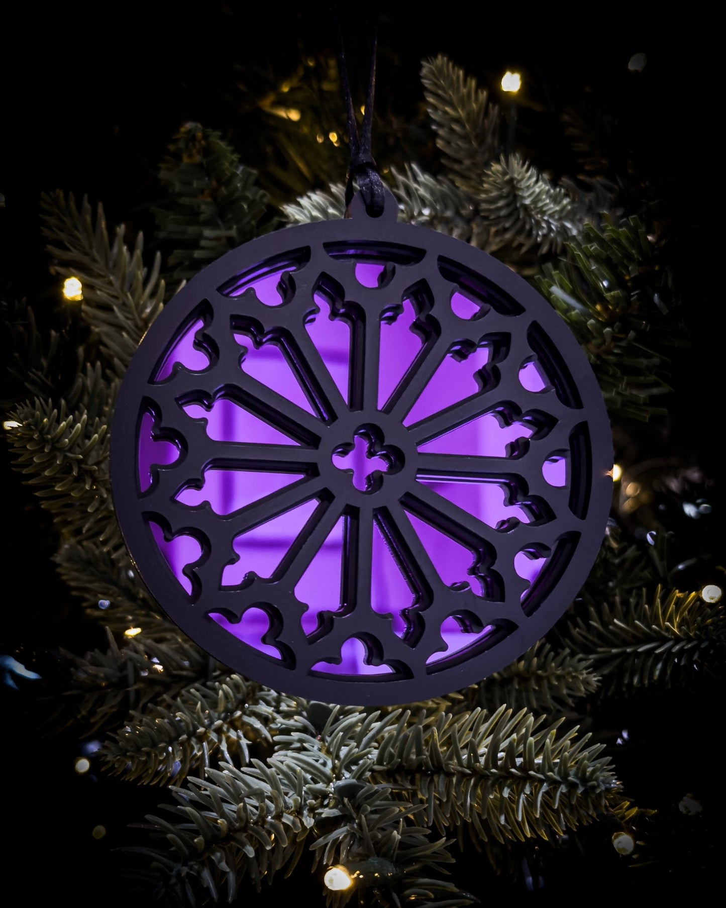 Purple gothic cathedral rose window ornament hanging on Christmas tree with warm lights