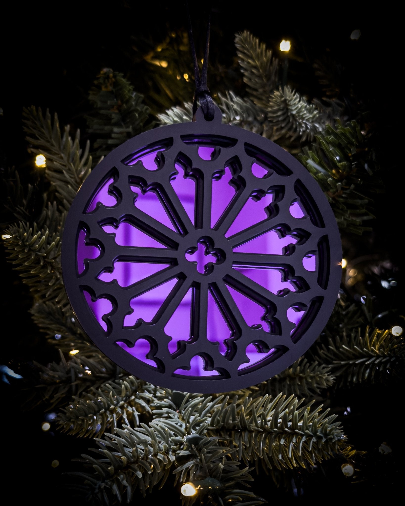 Purple gothic cathedral rose window ornament hanging on Christmas tree with warm lights