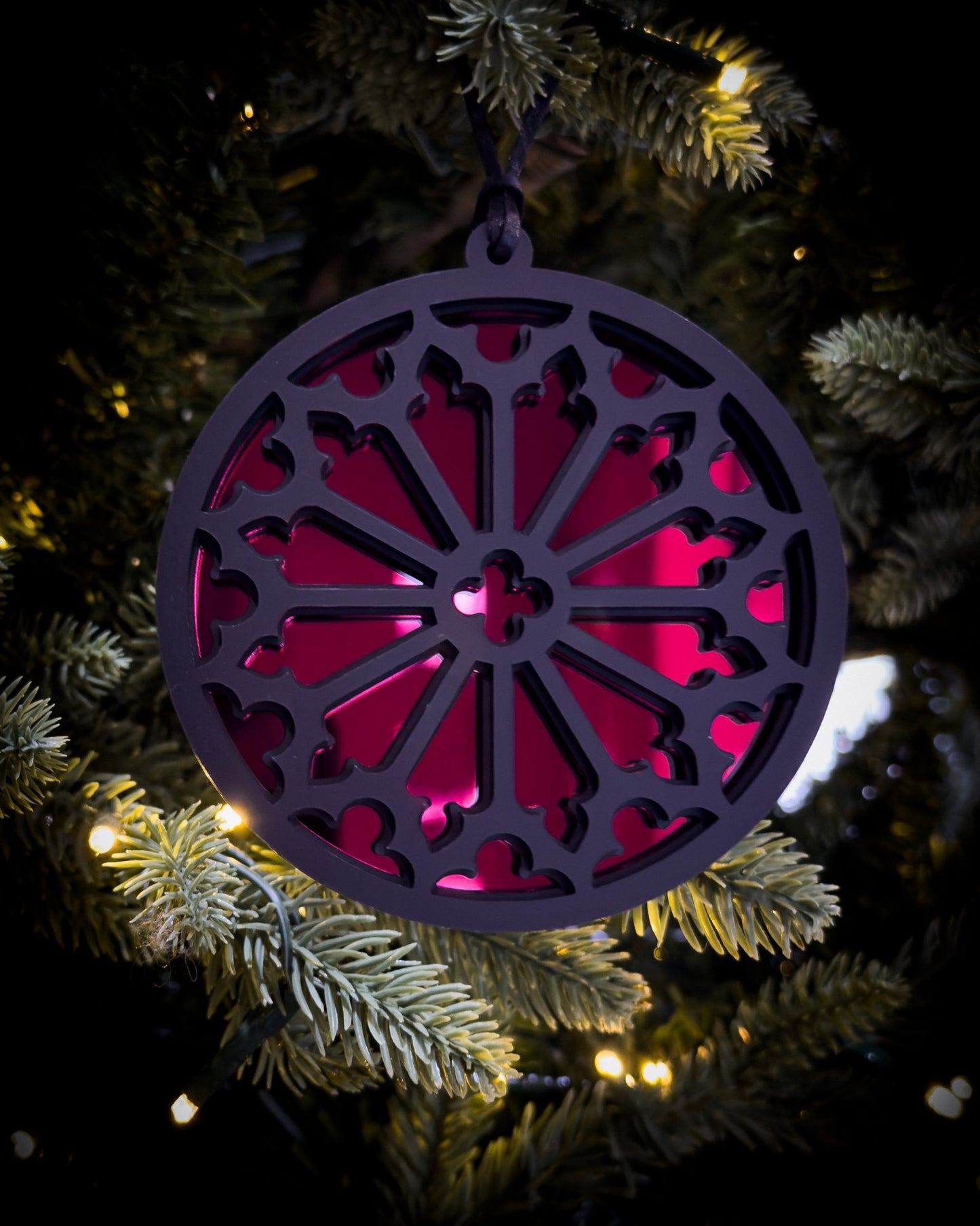Red gothic cathedral rose window ornament hanging on Christmas tree with warm lights