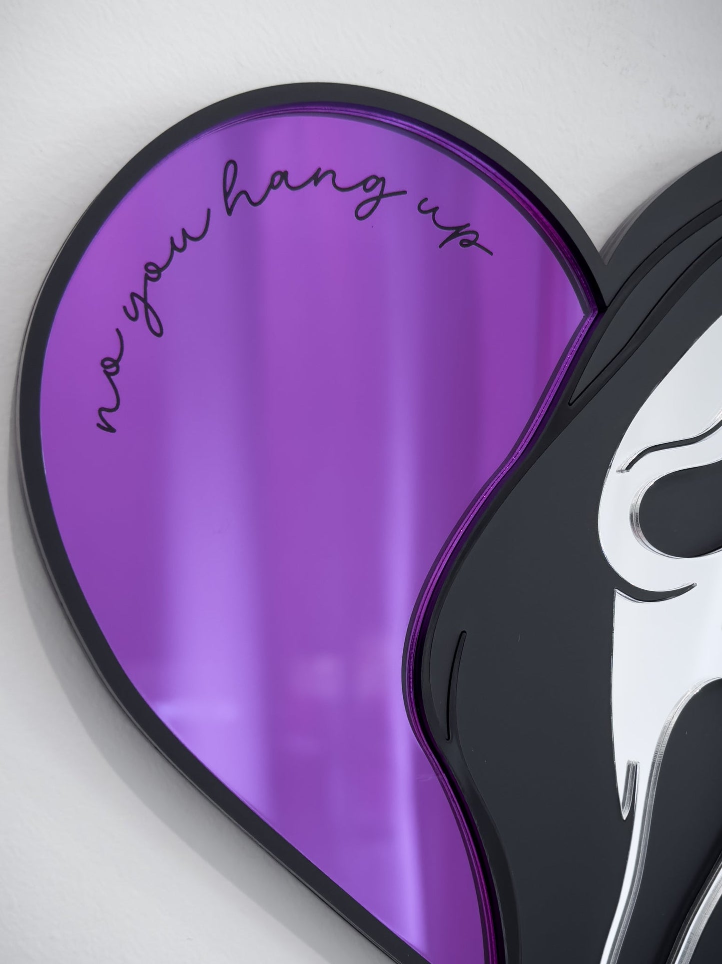 Close-up ghostface heart mirror with purple acrylic and engraved text “no you hang up” mounted on a white wall