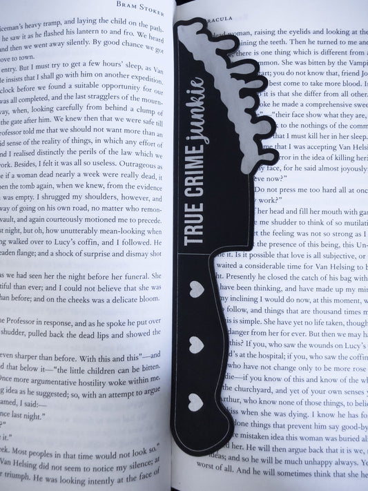 True crime junkie knife bookmark in black and silver  leatherette resting on an open book