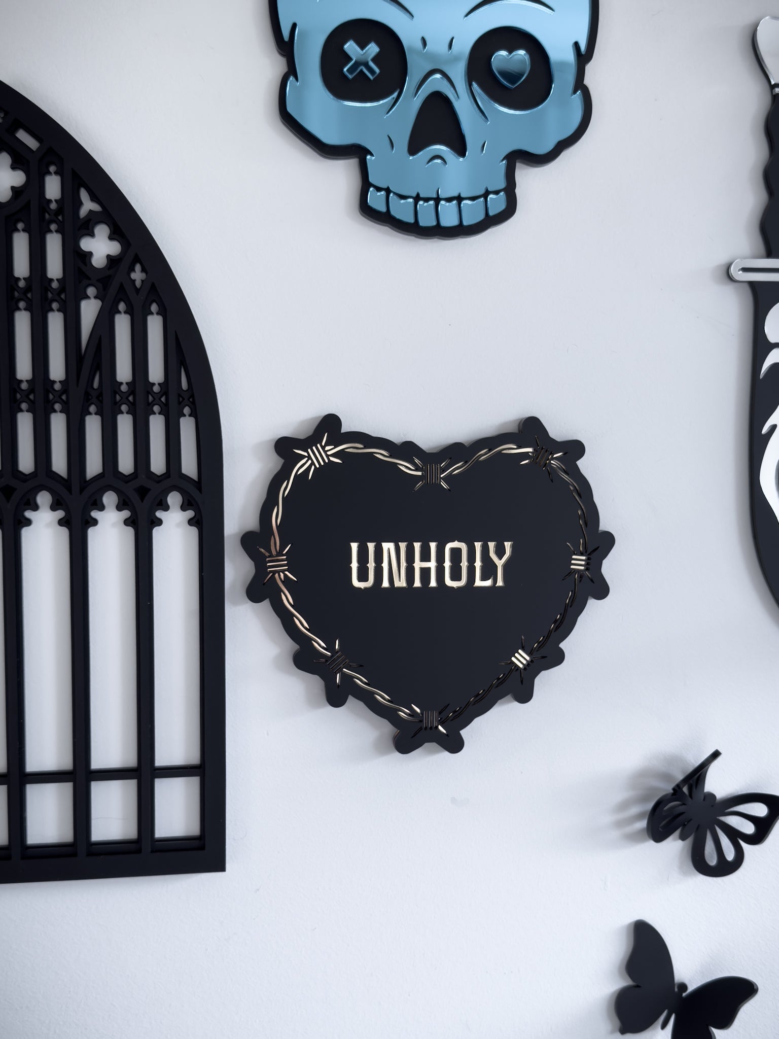 Close-up of gothic barbed wire heart wall art with “Unholy" text, styled in a gothic gallery wall