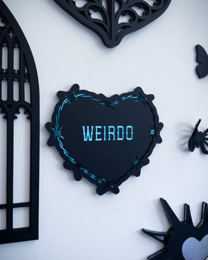 Close-up of gothic barbed wire heart wall art with “Weirdo” text, styled in a gothic gallery wall